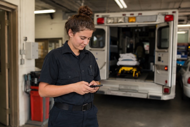 An EMT student checking the Impulse Test Prep app on their phone in an ambulance bay